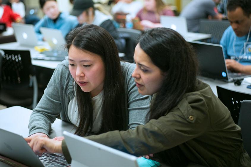 两个学生说话，都指着电脑屏幕.